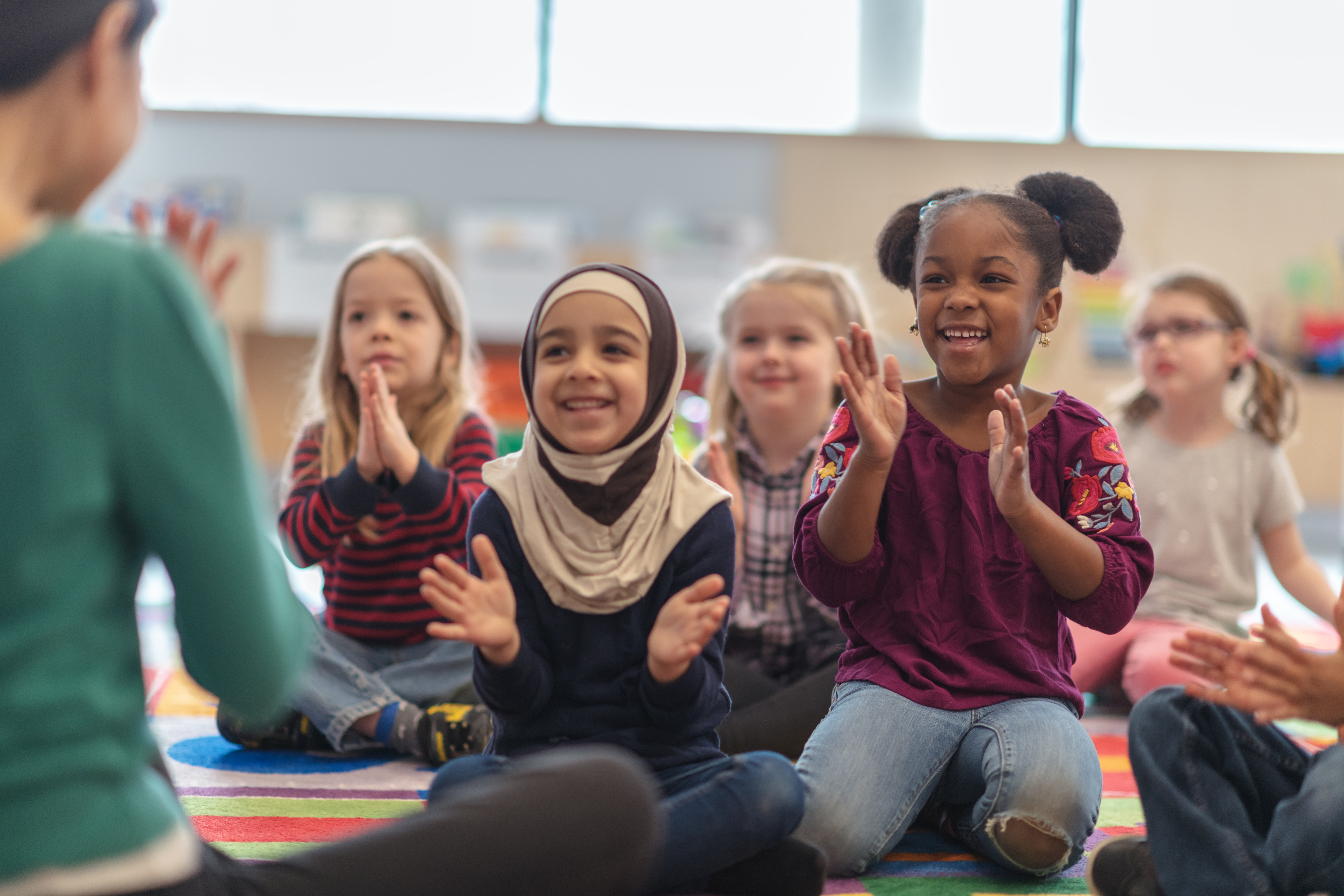 A group of children clapping along with a teacher during circle time.
